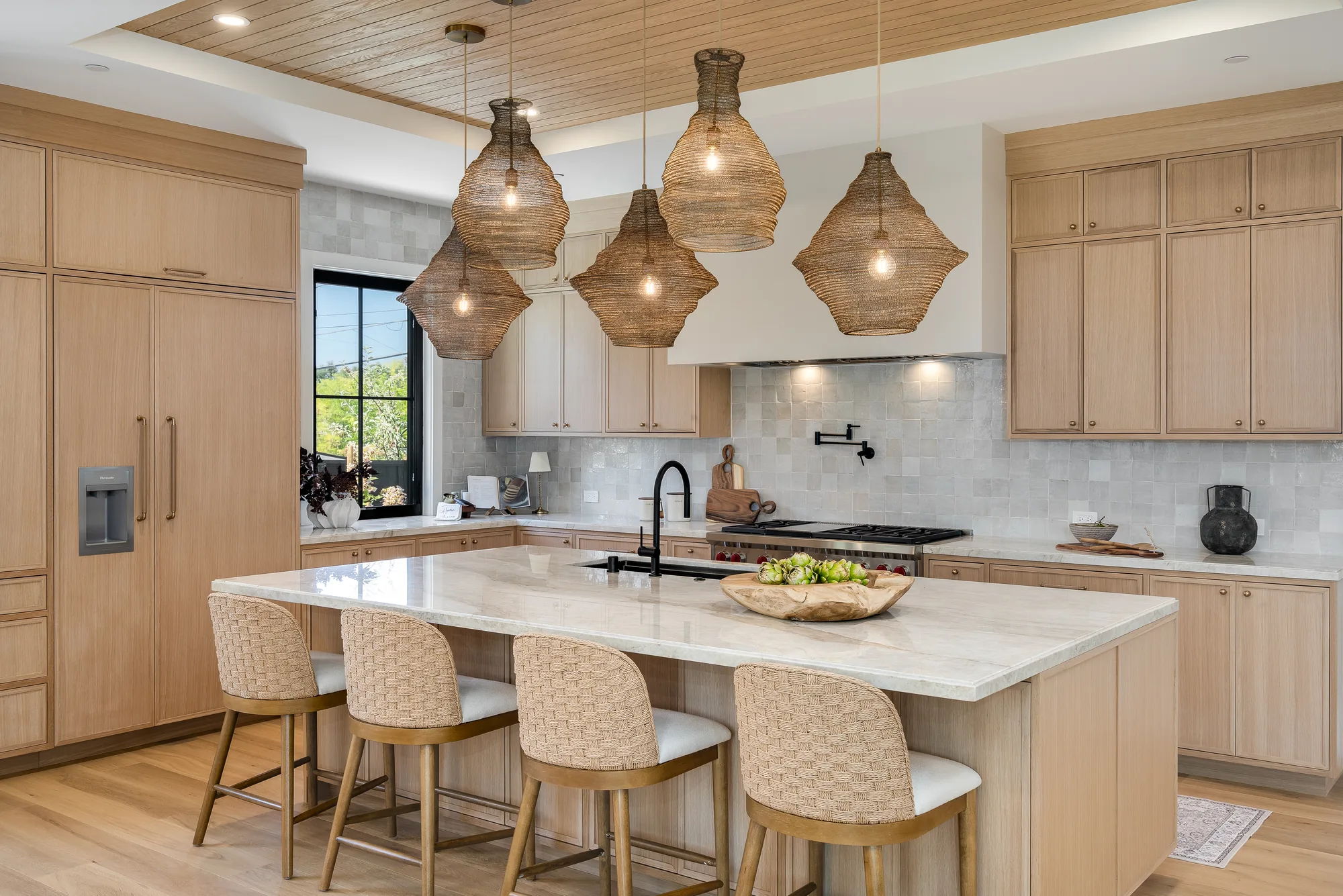 A finished kitchen: white oak cabinetry and a quartzite island under a run of woven pendant lights, woven counter stools along its length