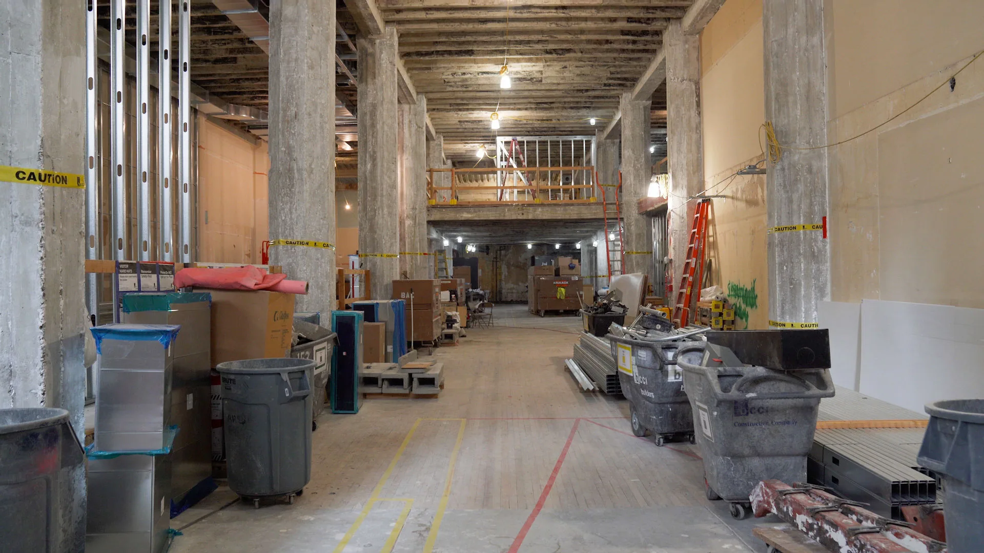 The Center for Architecture + Design mid-construction: concrete columns, exposed ceiling, framing and site protection down the gallery