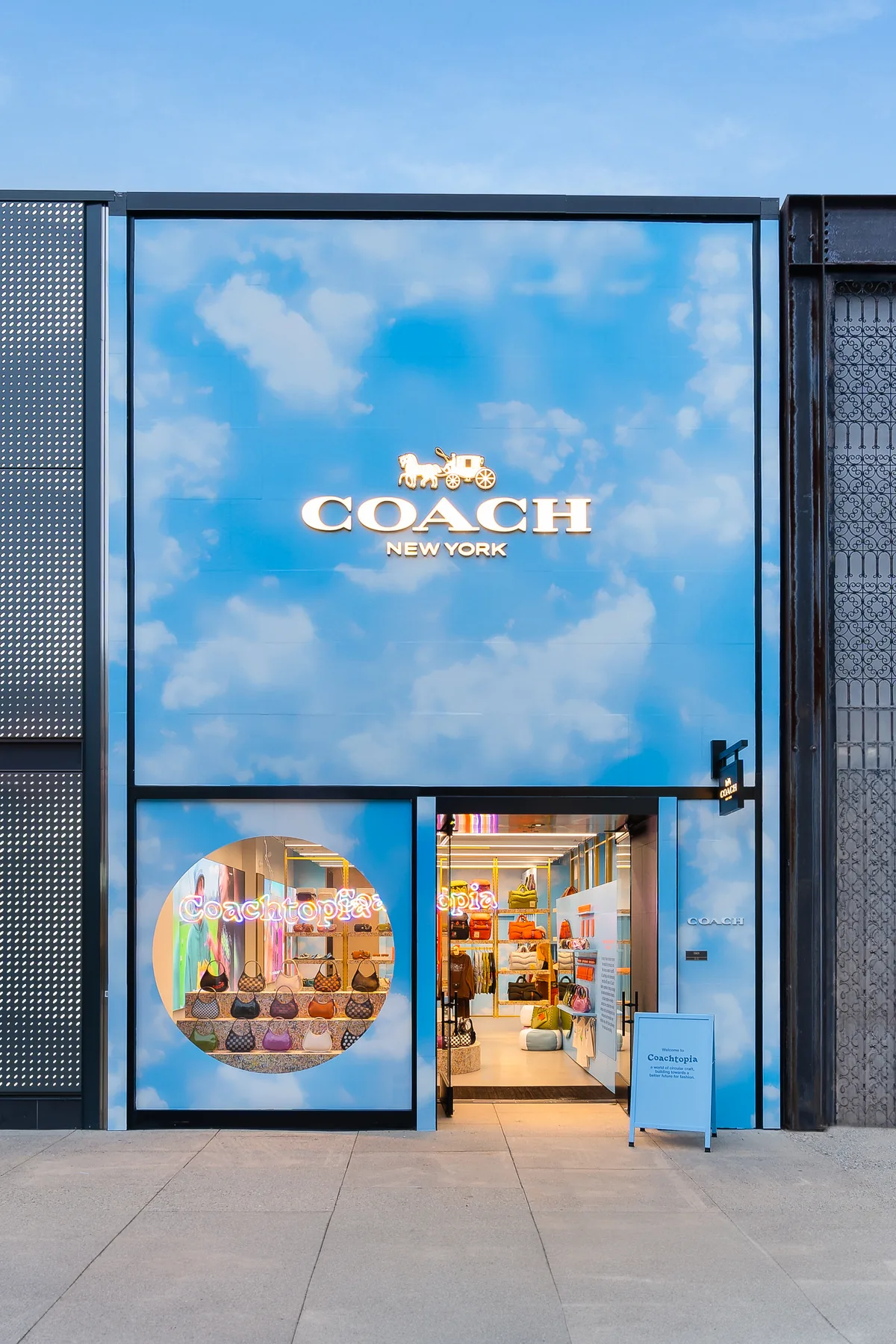 The Coachtopia storefront in Palo Alto: a sky-and-cloud printed facade under the Coach New York sign, bags arranged in a circular window