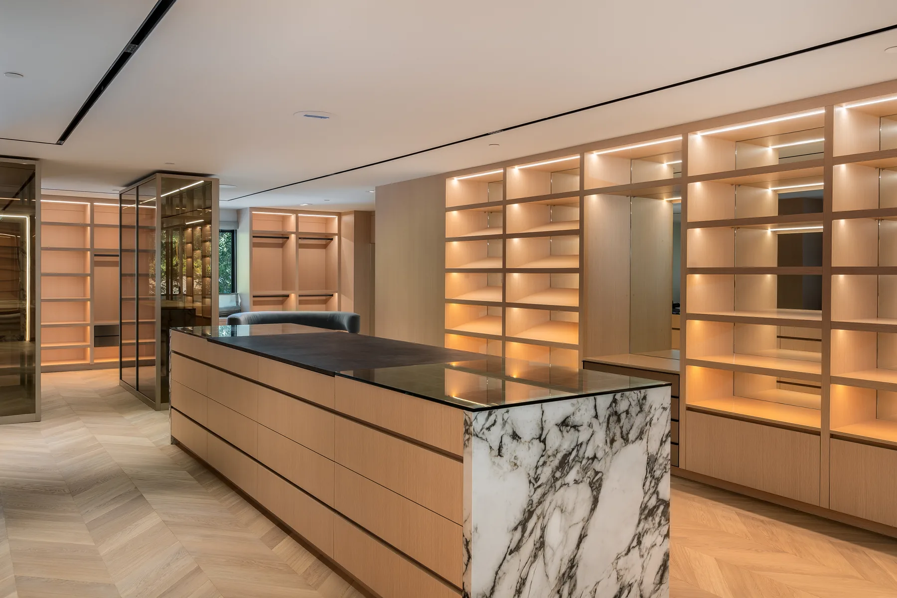 A Silicon Valley residence, dressing room: a marble-topped island under a full wall of backlit oak shelving