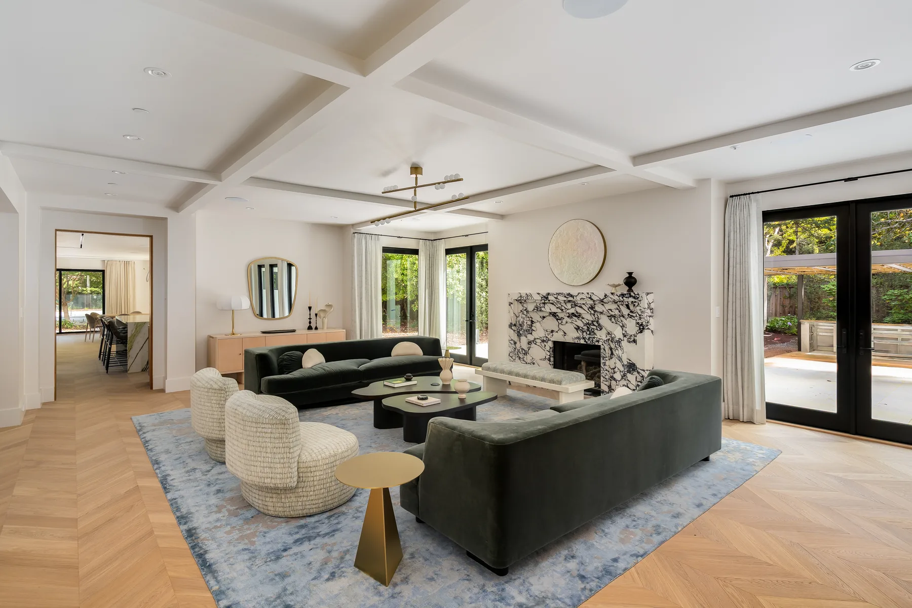 A Silicon Valley residence, living room: green sofas and a marble fireplace under a coffered ceiling, French doors down one wall and the dining room beyond