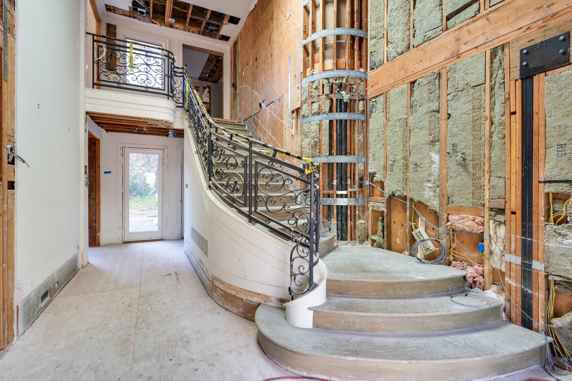 A staircase stripped back to studs, standing alone against open framing and insulation where the walls had been