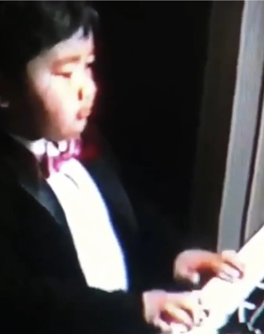 Mike at three, in a tuxedo, playing the piano.