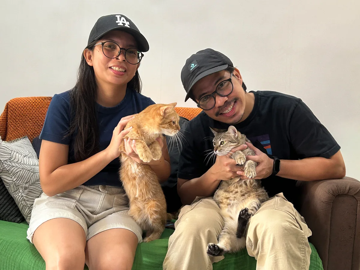 Nico and a friend on a green couch, each holding up a cat.