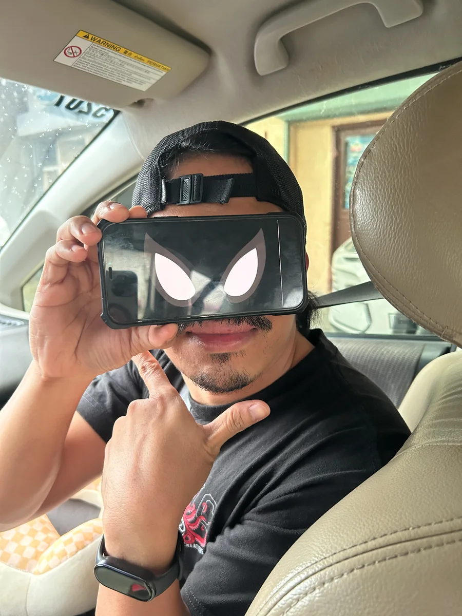 Nico in a car, holding a phone with a masked-hero screen over his eyes.