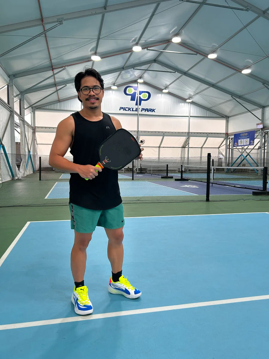 Nico on a pickleball court, paddle in hand, under a Pickle Park sign.