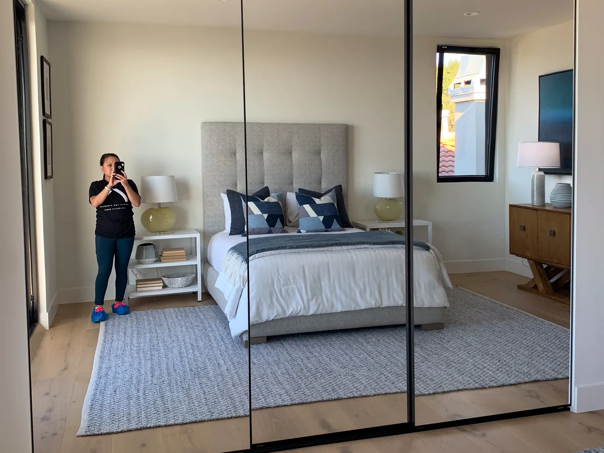 Rachel photographing a staged bedroom, caught in its mirrored closet doors.